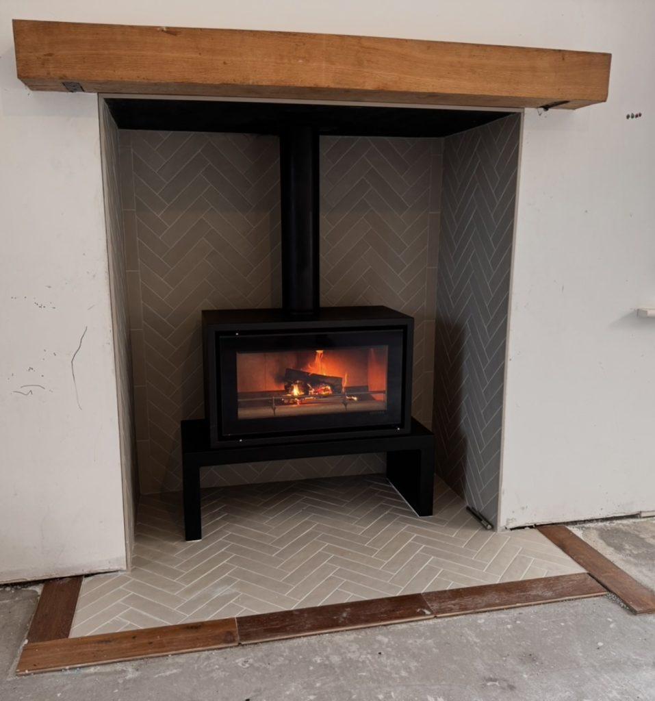 Stovax Studio 2 freestanding stove on a Stovax bench, lit, with a custom herringbone tiled hearth and herringbone tiled chamber, Co. Meath